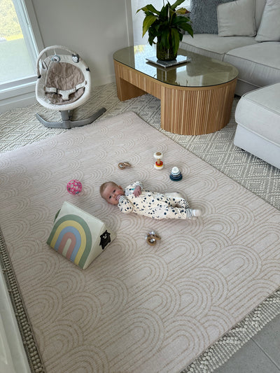 Baby lying on a large Arch-pattern play mat with toys and a mirror in a living room