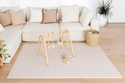 Large River Bend-pattern play mat with a wooden play gym, toy balls and woven basket in front of a cream sofa