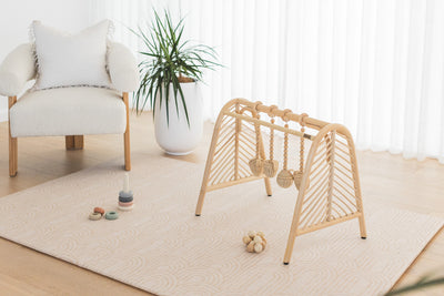 Arch / River Bend play mat with a wooden play gym and stacking toys beside a white armchair