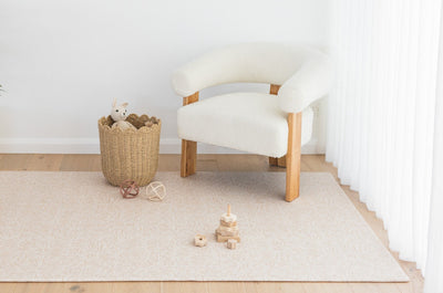 Arch / River Bend play mat beneath a white armchair, with a woven toy basket and wooden stacking toys