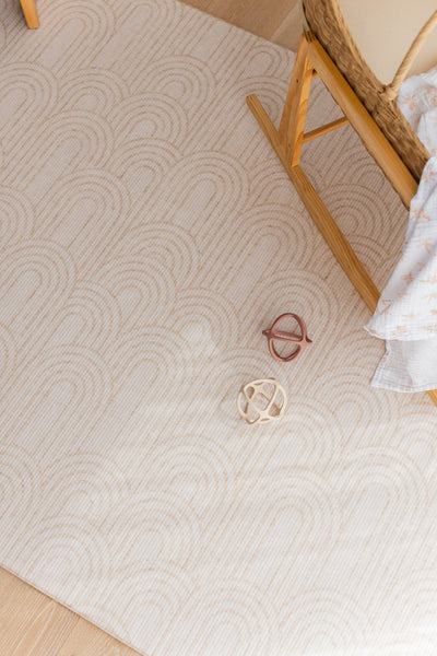 Overhead close-up of the Arch play mat pattern beside a wooden bassinet stand and two toy balls