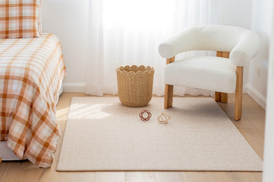 River Bend-pattern play mat beside gingham-covered furniture, with a white armchair, woven basket and toy balls