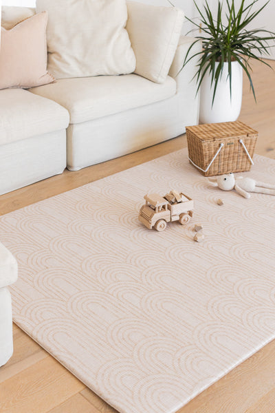 Arch-pattern play mat with a wooden toy truck and soft rabbit beside a cream sofa