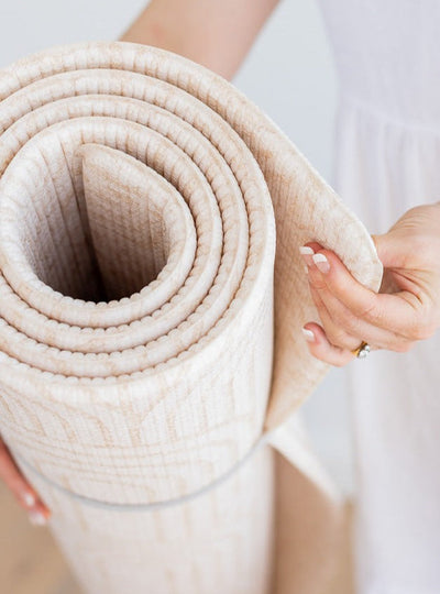 Close-up of a rolled Arch / River Bend play mat, with a hand holding its curved edge