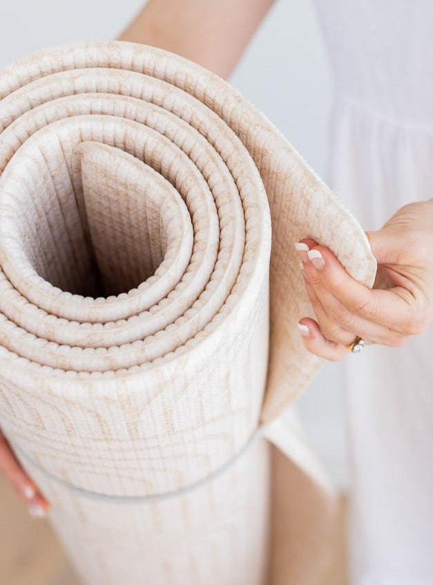 Close-up of a rolled Arch / River Bend play mat, with a hand holding its curved edge