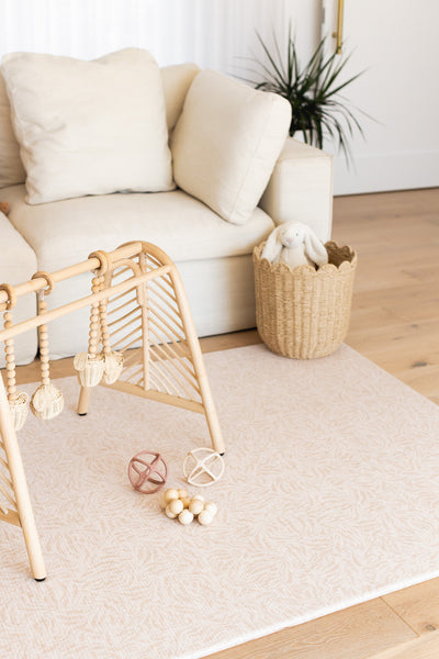 River Bend-pattern baby play mat with a wooden play gym and toy balls beside a cream sofa