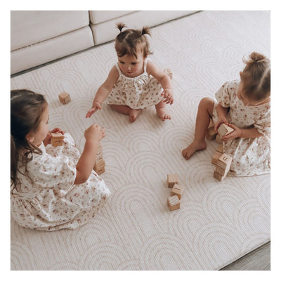 Three children playing with wooden blocks on the Arch-pattern baby play mat beside a sofa